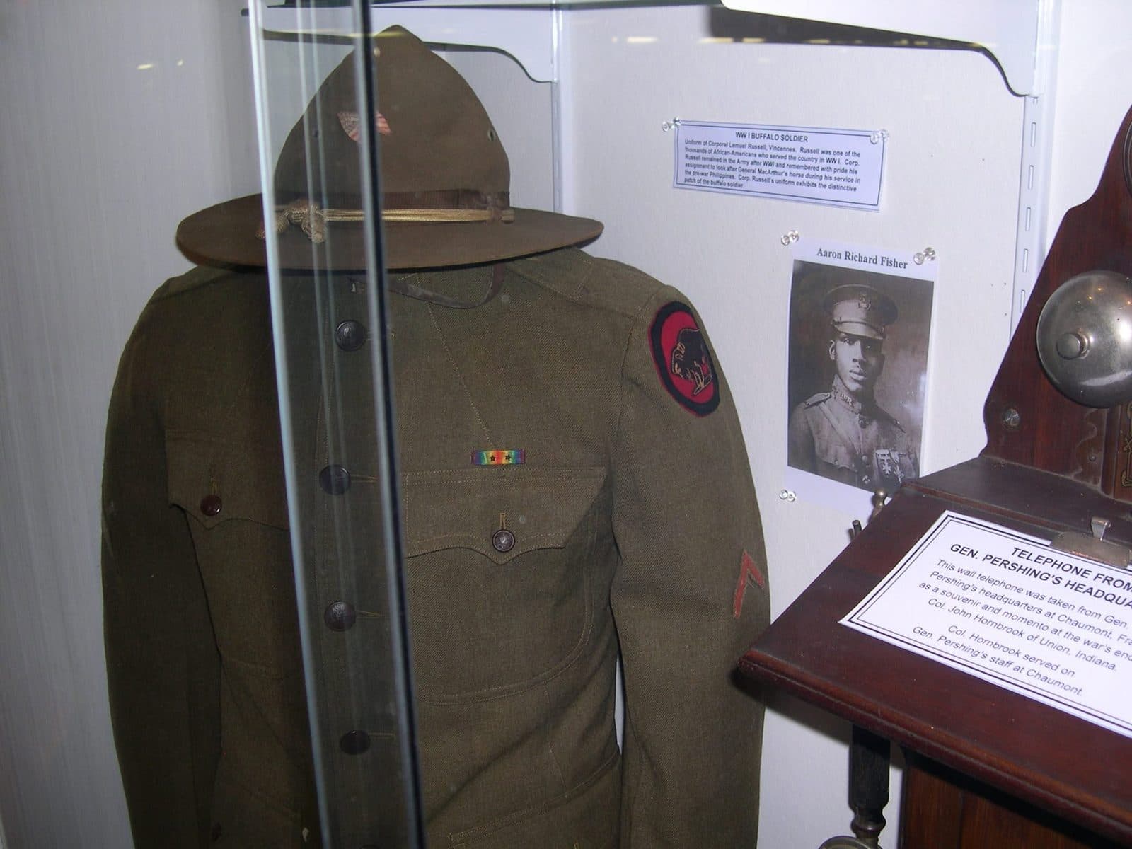 Close view of a museum display case showing a campaign hat and uniform jacket with a shoulder patch, beside a "WWI Buffalo Soldier" placard and a photograph of a soldier.