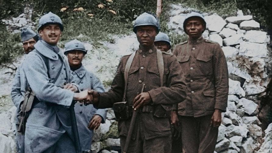 Colorized historical photograph of a French soldier in a horizon-blue uniform shaking hands with an American Black soldier, with other soldiers standing near a stone wall.