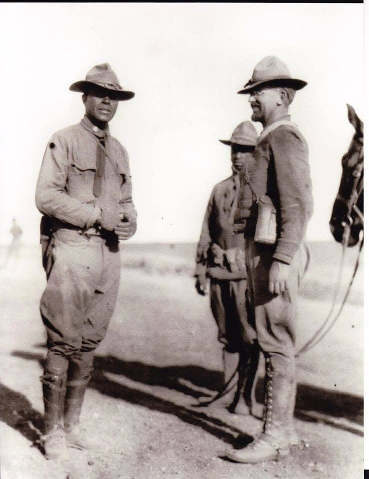 Black-and-white photograph of three men in campaign hats standing beside a horse in an open field.