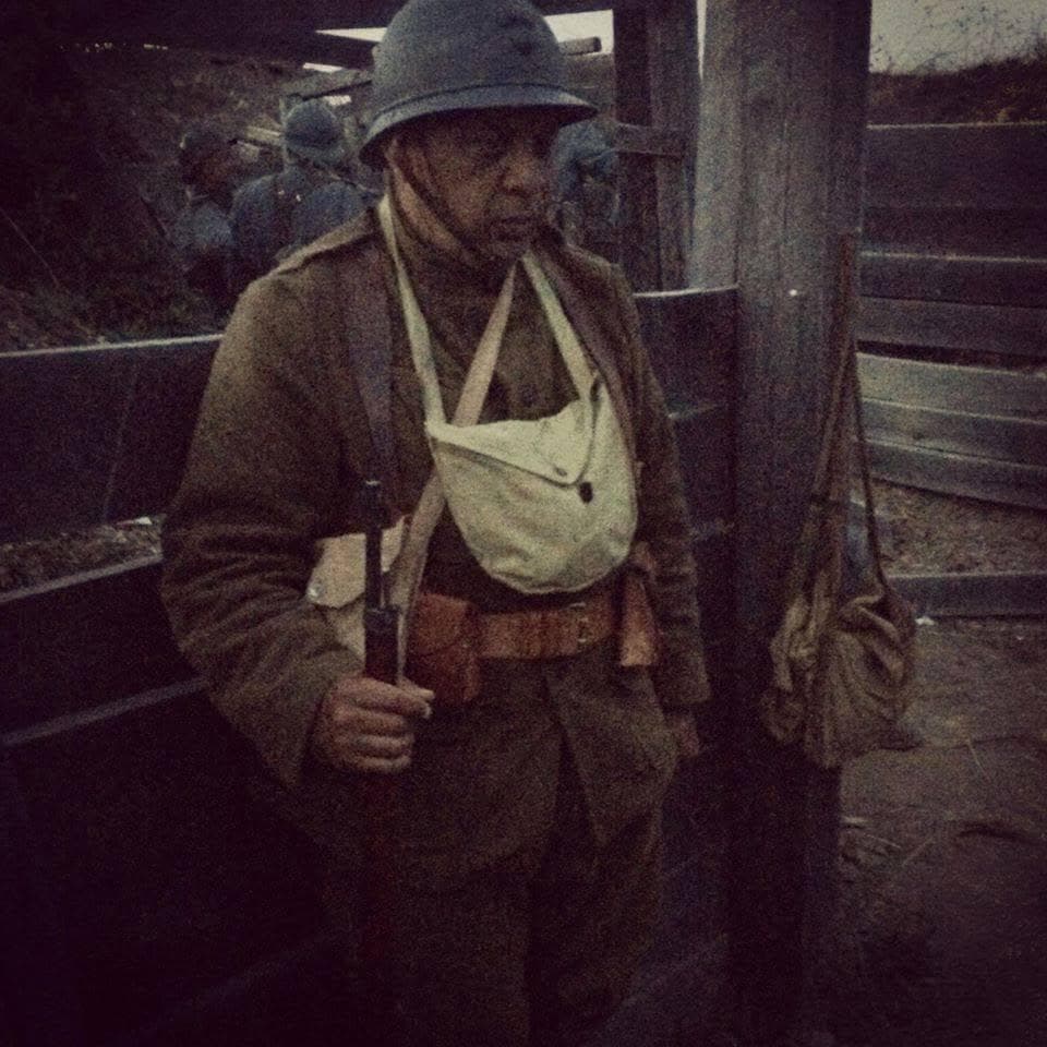 Dimly lit modern color photograph, close portrait of a reenactor wearing a white arm sling bandage over his uniform, holding a fixed-bayonet rifle.