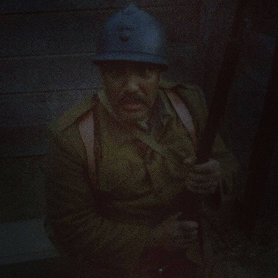 Dimly lit modern color photograph of a reenactor in a helmet, smiling faintly, holding a rifle.