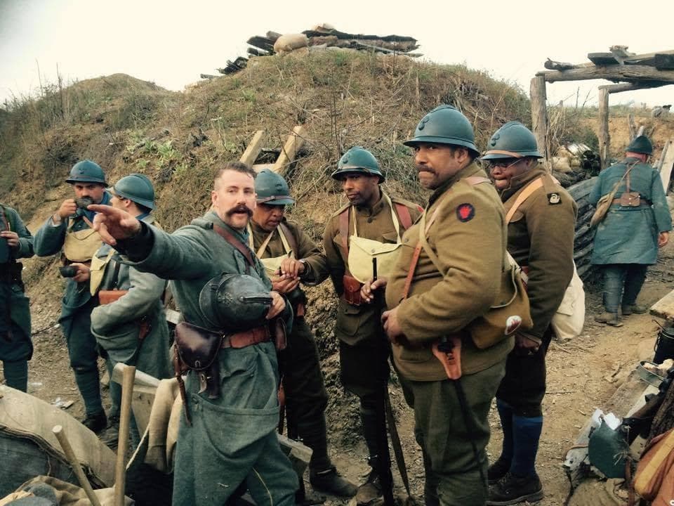 Modern color photograph of seven reenactors gathered near a dugout mound topped with sandbags and log revetments, one man pointing toward the camera.