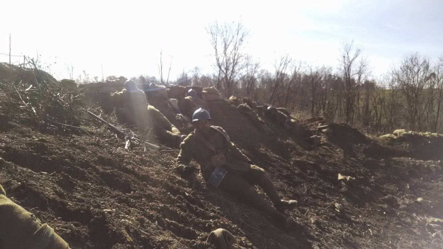 Modern color photograph of a single reenactor reclining on a dirt embankment beside sandbags, looking toward the camera.