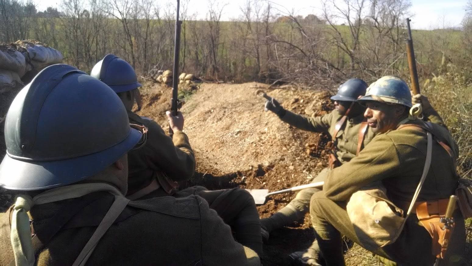 Modern color photograph of reenactors in French Adrian helmets in a dug trench, one gesturing toward the tree line.