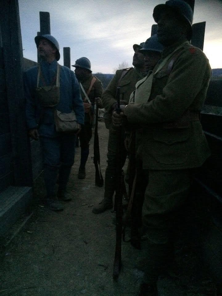 Dim twilight color photograph of reenactors in mixed blue and khaki uniforms standing at a wood-framed dugout entrance.